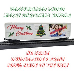 May include: A white model train boxcar with a red and green Merry Christmas design and a Christmas tree. The boxcar has a photo area that says 