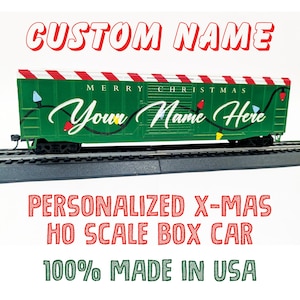 May include: A green and red personalized HO scale box car with the text "Merry Christmas" and "Your Name Here" on the side. The car has a white and red striped roof and is decorated with lights.