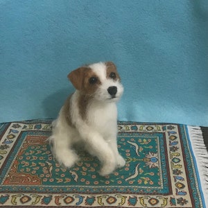May include: A white and brown needle felted Jack Russell Terrier dog sitting on a colorful patterned rug.