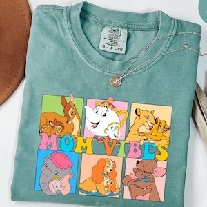 May include: A light green t-shirt with a vintage wash featuring a colorful graphic of Disney characters with the text "Mom Vibes".