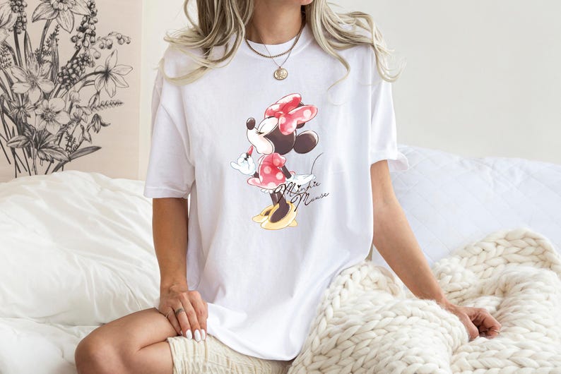 Puede incluir: Camiseta blanca de gran tama&ntilde;o con un estampado gr&aacute;fico de Minnie Mouse con un vestido rojo con lunares blancos y un lazo rojo. El texto "Minnie Mouse" est&aacute; impreso debajo del gr&aacute;fico.