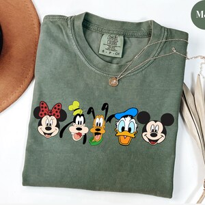 May include: A green t-shirt with a graphic of Mickey Mouse, Minnie Mouse, Goofy, Pluto, and Donald Duck. The shirt has the text "Comfort Colors" on the tag.