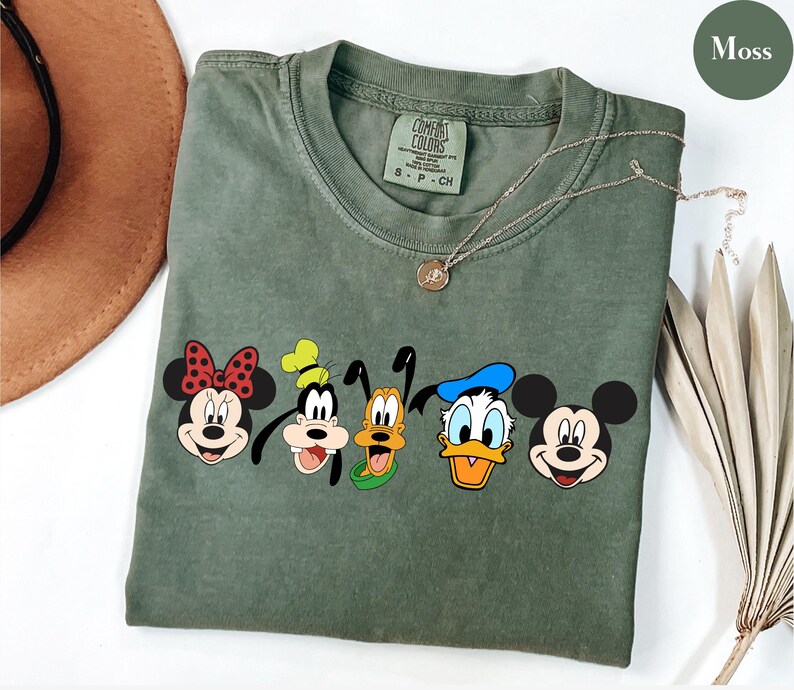 May include: A green t-shirt with a graphic of Mickey Mouse, Minnie Mouse, Goofy, Pluto, and Donald Duck. The shirt has the text "Comfort Colors" on the tag.