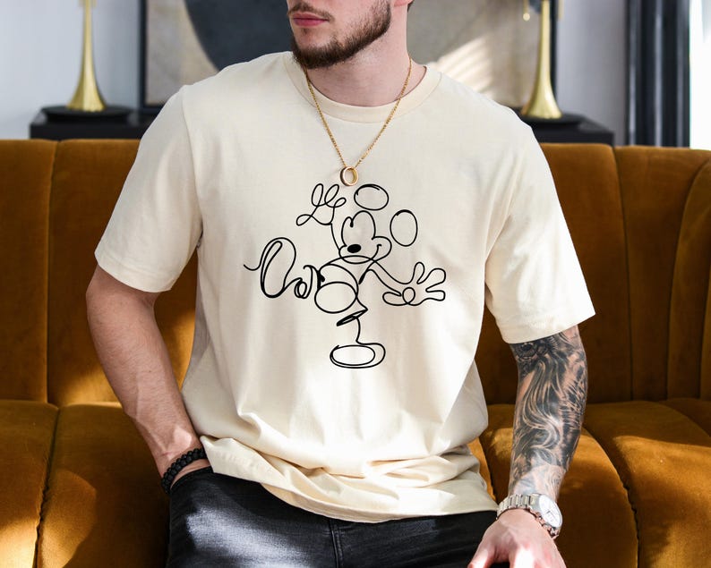 Puede incluir: Una camiseta blanca con un dibujo de l&iacute;nea negra de Mickey Mouse haciendo malabares con c&iacute;rculos.