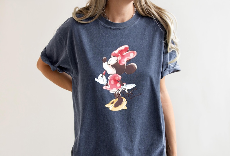 Puede incluir: Una camiseta azul oscuro con un gr&aacute;fico de Minnie Mouse con un lazo rojo y sosteniendo un l&aacute;piz labial. El gr&aacute;fico es de estilo vintage.