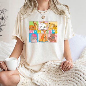 May include: A white t-shirt with a graphic print of Disney characters in colorful squares. The text "MOM VIBES" is printed in a colorful font across the squares.