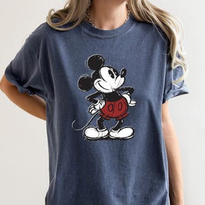 May include: A dark blue t-shirt with a vintage-style image of Mickey Mouse in black and white. Mickey is wearing red shorts and is looking to the right.