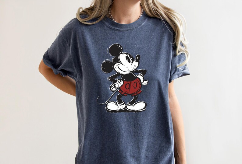 May include: A dark blue t-shirt with a vintage-style image of Mickey Mouse in black and white. Mickey is wearing red shorts and is looking to the right.