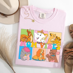 May include: Pink t-shirt with a graphic of Disney characters and the text "MOM VIBES". The characters include Bambi, Belle, Simba, Dumbo, Lady, and Winnie the Pooh.