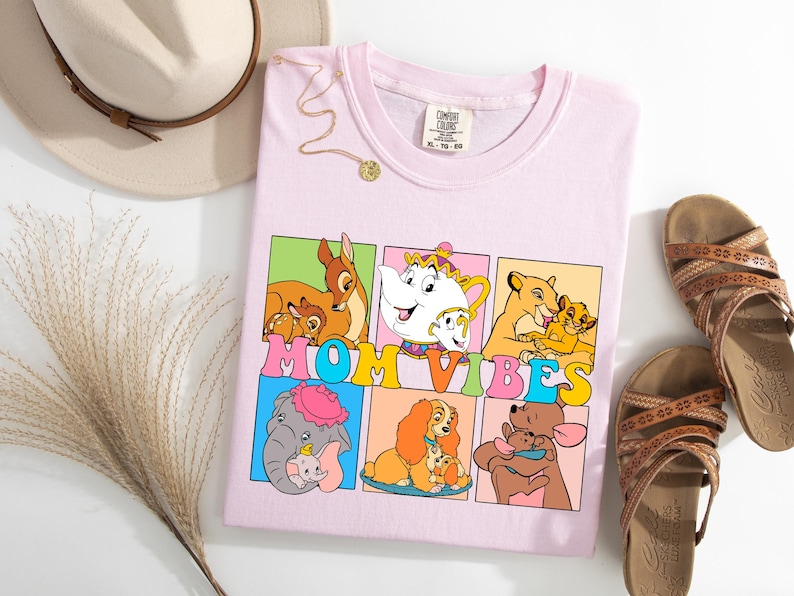 May include: Pink t-shirt with a graphic of Disney characters and the text "MOM VIBES". The characters include Bambi, Belle, Simba, Dumbo, Lady, and Winnie the Pooh.