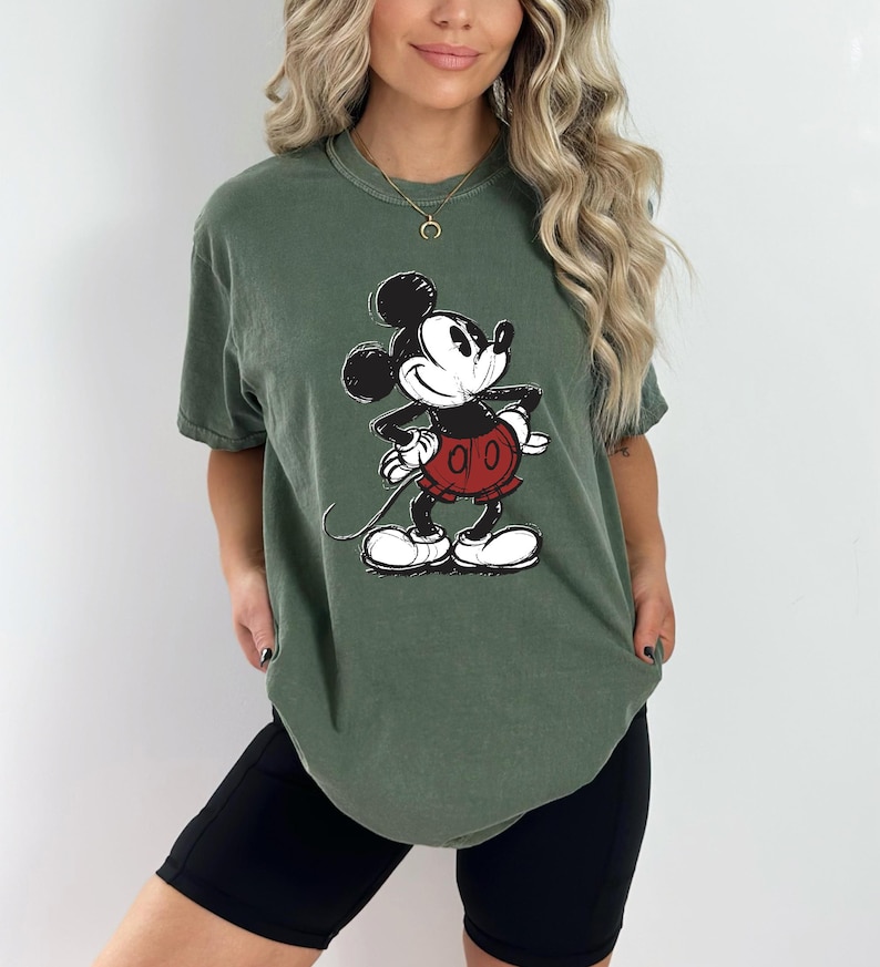 May include: A green t-shirt with a vintage Mickey Mouse graphic. The shirt has a relaxed fit and short sleeves.