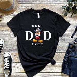 Op de afbeelding: Zwart T-shirt met een witte afbeelding van Mickey Mouse met een zonnebril en een petje achterstevoren. De tekst "BEST DAD EVER" staat onder de afbeelding.