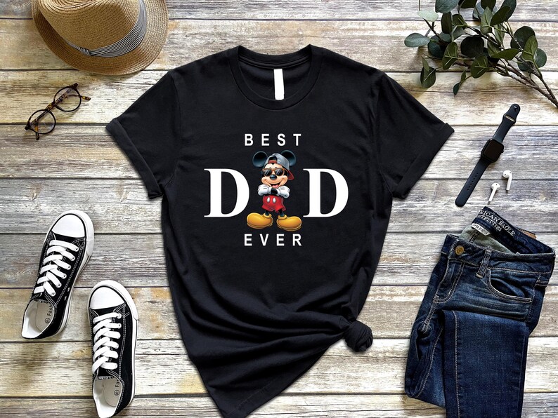 Op de afbeelding: Zwart T-shirt met een witte afbeelding van Mickey Mouse met een zonnebril en een petje achterstevoren. De tekst "BEST DAD EVER" staat onder de afbeelding.