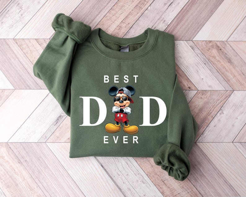 Op de afbeelding: Groen sweatshirt met een witte afbeelding van Mickey Mouse met een zonnebril en de tekst "BEST DAD EVER".