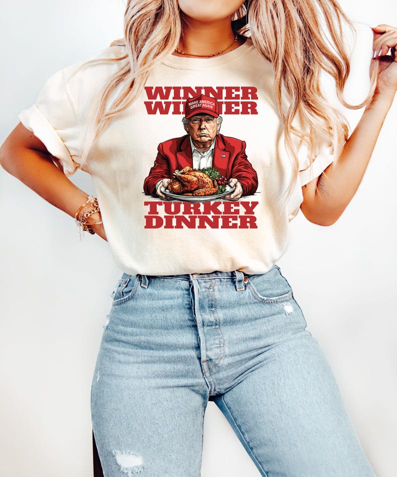 May include: A white t-shirt with a red, white, and blue graphic of a man wearing a red "Make America Great Again" hat holding a turkey. The text "Winner Winner Turkey Dinner" is printed in red on the shirt.