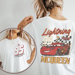 May include: A white t-shirt featuring a graphic of the red race car Lightning McQueen from the film Cars. The back design includes the number 95, a chequered flag, and the text Lightning McQueen. The front chest area displays the number 95.