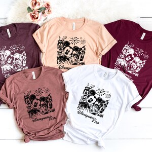K&ouml;nnte beinhalten: F&uuml;nf verschiedene T-Shirts mit einem schwarz-wei&szlig;en Grafikdruck von Mickey Mouse und seinen Freunden. Die Shirts sind in verschiedenen Farben, darunter Rotbraun, Beige, Wei&szlig; und Rosa. Der Text "Disneyworld 2023" ist auf den Shirts gedruckt.