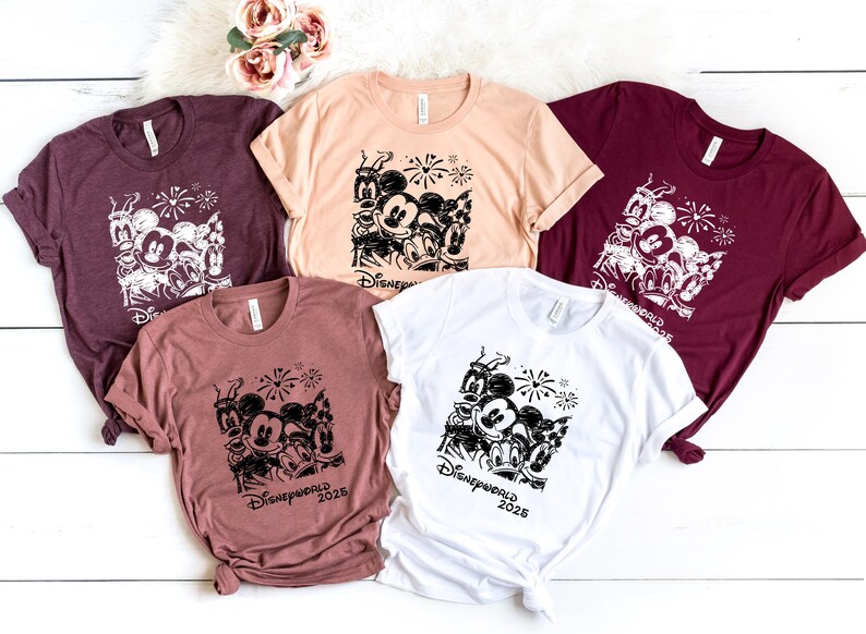 K&ouml;nnte beinhalten: F&uuml;nf verschiedene T-Shirts mit einem schwarz-wei&szlig;en Grafikdruck von Mickey Mouse und seinen Freunden. Die Shirts sind in verschiedenen Farben, darunter Rotbraun, Beige, Wei&szlig; und Rosa. Der Text "Disneyworld 2023" ist auf den Shirts gedruckt.