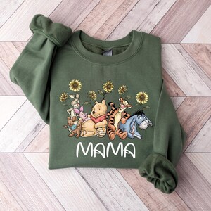 Puede incluir: Sudadera verde con un gr&aacute;fico de Winnie de Pooh y sus amigos, incluyendo Piglet, Tigger, Eeyore y Rabbit. El gr&aacute;fico incluye girasoles y la palabra "MAMA" impresa debajo de los personajes.