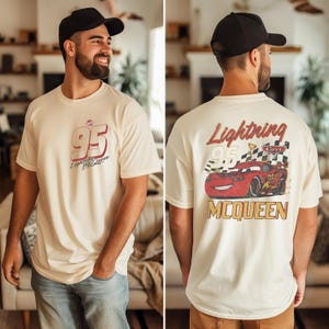 May include: An off-white short-sleeve t-shirt featuring a small red and black number 95 graphic on the front chest. The back displays a large illustration of a red race car with the text Lightning McQueen, the number 95, and a checkered flag.