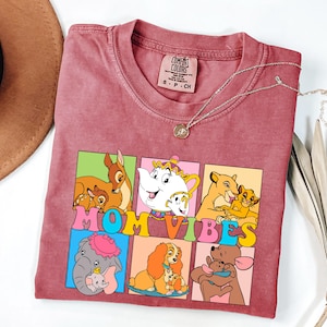 May include: A red t-shirt with a graphic of Disney characters and the text "MOM VIBES". The characters include Bambi, Dumbo, Lady, Simba, and the Beast.