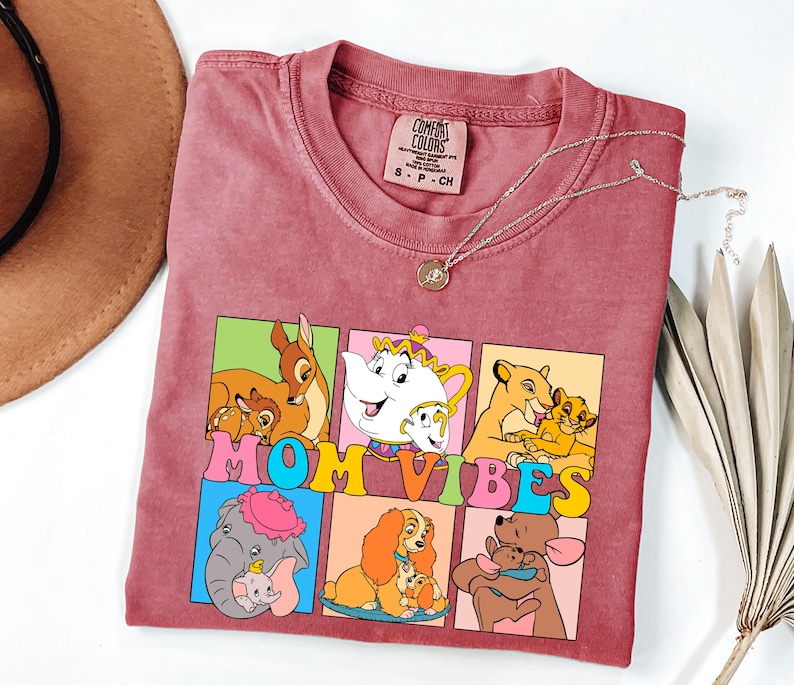 May include: A red t-shirt with a graphic of Disney characters and the text "MOM VIBES". The characters include Bambi, Dumbo, Lady, Simba, and the Beast.