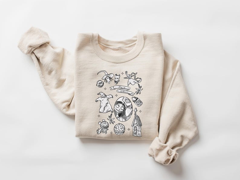 K&ouml;nnte beinhalten: Ein cremefarbenes Sweatshirt mit einem schwarz-wei&szlig;en Grafikdesign. Das Design zeigt verschiedene Charaktere und Elemente aus einem beliebten Animationsfilm, wie einen Hexenhut, einen Geist und ein Charakterportr&auml;t. Das Sweatshirt hat lange &Auml;rmel.