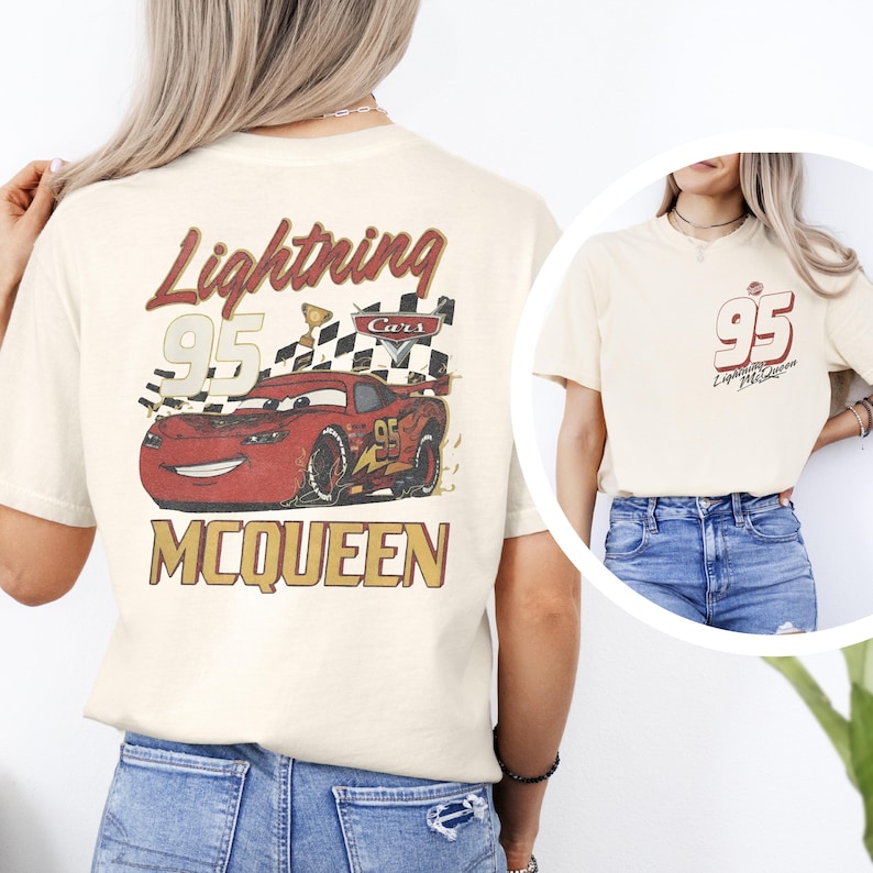 May include: A cream-coloured t-shirt featuring a graphic of a red race car with the number 95, a checkered flag, and the text Lightning McQueen on the back. The front chest area displays the number 95 and the text Lightning McQueen in red.