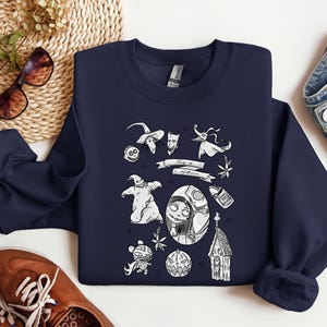 K&ouml;nnte beinhalten: Marineblaues Sweatshirt mit einem wei&szlig;en Grafikdesign von Charakteren und Elementen aus "The Nightmare Before Christmas". Das Design umfasst Jack Skellington, Sally, Zero und andere ikonische Bilder. Der Text "This is Halloween" ist ebenfalls vorhanden.