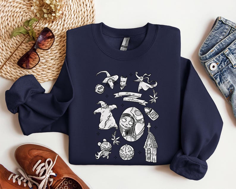 K&ouml;nnte beinhalten: Marineblaues Sweatshirt mit einem wei&szlig;en Grafikdesign von Charakteren und Elementen aus "The Nightmare Before Christmas". Das Design umfasst Jack Skellington, Sally, Zero und andere ikonische Bilder. Der Text "This is Halloween" ist ebenfalls vorhanden.