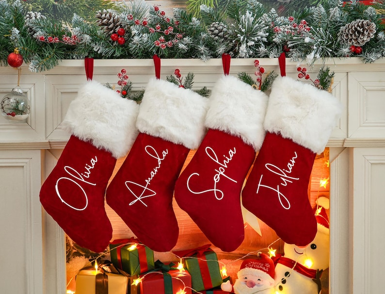 May include: Four red Christmas stockings with white faux fur trim and personalized names: Olivia, Amanda, Sophia, and Julian.