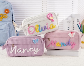 May include: Three corduroy pencil cases in white, lavender, and pink, each with a name embroidered in colorful thread. The white case has a lollipop and the name "Olivia". The lavender case has a butterfly and the name "Nancy". The pink case has a bow and the name "Mandy".