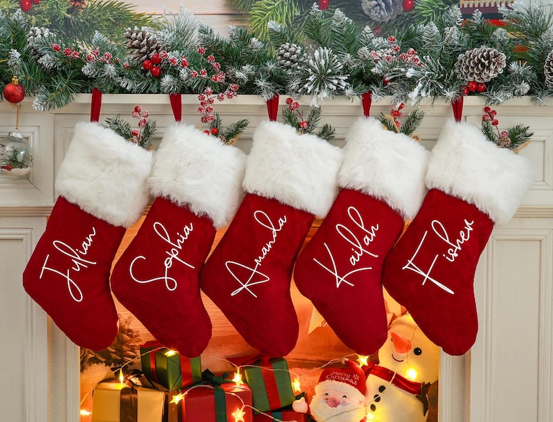 May include: Five red velvet Christmas stockings with white faux fur trim and personalized names in white script:  'Julian', 'Sophia', 'Amanda', 'Kaileah', and 'Fischer'.
