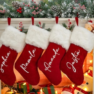 May include: Four red velvet Christmas stockings with white faux fur trim, hanging on a fireplace mantel. Each stocking is personalized with a name in white script: Sophia, Pamela, Amanda, and Justin.