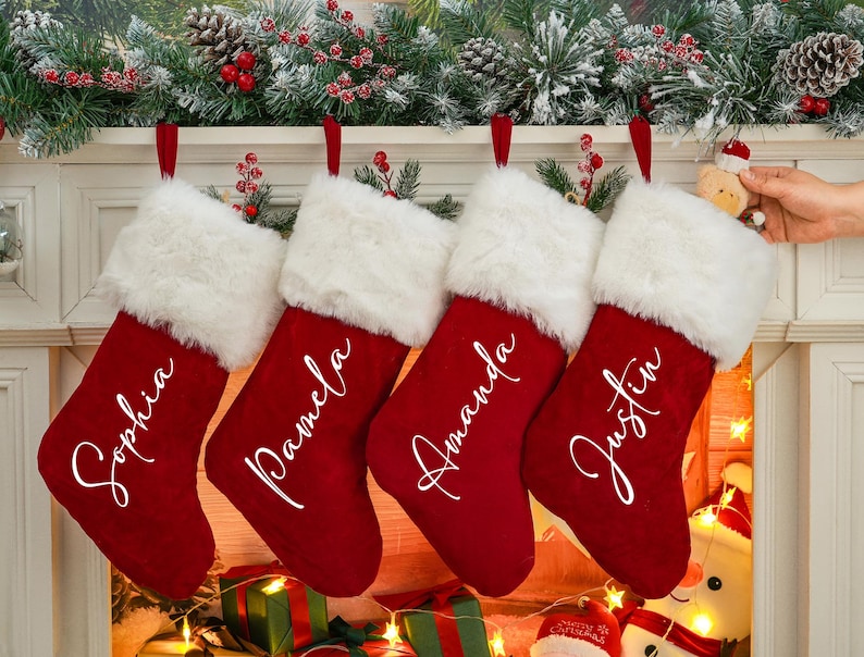 May include: Four red velvet Christmas stockings with white faux fur trim, hanging on a fireplace mantel. Each stocking is personalized with a name in white script: Sophia, Pamela, Amanda, and Justin.