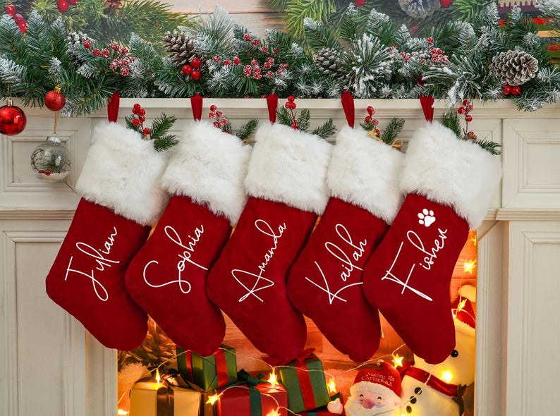 May include: Five red Christmas stockings with white faux fur trim hanging on a fireplace mantel. Each stocking is personalized with a name in white script:  "Jillian", "Sophia", "Amanda", "Kailah", and "Fisher".