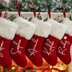 May include: Five red velvet Christmas stockings with white faux fur trim and personalized names in white script. The names are "Julian", "Sophia", "Amanda", "Kailan", and "Rocky".