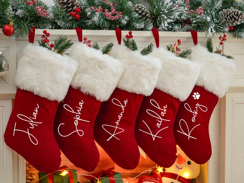May include: Five red velvet Christmas stockings with white faux fur trim and personalized names in white script. The names are "Julian", "Sophia", "Amanda", "Kailan", and "Rocky".
