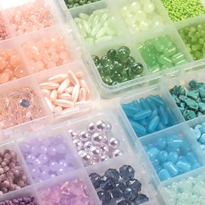 May include: A clear plastic organiser filled with a variety of colourful beads. The beads are in shades of pink, peach, green, blue, and purple. Bead shapes include round, oval, and faceted, ideal for jewellery making and crafting.
