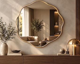 May include: A large, wall-mounted mirror with an organic, wavy gold frame. The mirror reflects a living room interior. It is positioned above a long, horizontal, dark wood floating console table that features three drawers and a smooth surface.