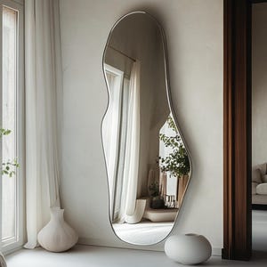 May include: A large, free-form, silver-framed mirror with a white background. The mirror is reflecting a room with white curtains and a plant.