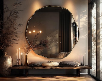 May include: A large, round, organic-shaped wall mirror with a thin black frame. The mirror reflects a room interior with warm lighting, and it is positioned above a long, dark wooden bench holding decorative pillows and candles.