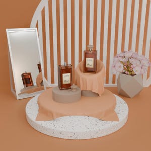 May include: A still-life composition featuring two rectangular perfume bottles with the text "Coco" and "Pharja" on the labels. The bottles are displayed on a round platform with a peach-colored cloth, alongside a mirror and a geometric vase with pink flowers.