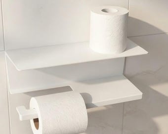 May include: A white metal wall-mounted toilet paper holder featuring a flat upper shelf and a lower horizontal bar for a roll. The unit holds one roll of toilet paper on the bar and one additional roll resting on the top shelf surface.