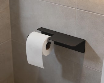 May include: A matte black metal toilet roll holder featuring a flat rectangular shelf on top. The holder is mounted horizontally and supports a single roll of white toilet paper, which hangs from the integrated arm extending from the shelf.