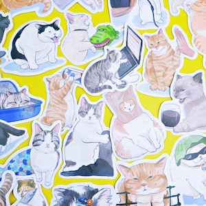 Puede incluir: Una colección de pegatinas con temática de gatos sobre un fondo amarillo. Las pegatinas presentan varias ilustraciones de gatos en diferentes poses y actividades, incluyendo gatos con portátiles, sosteniendo peces y usando gafas de sol. Los gatos están representados en una variedad de colores y patrones.
