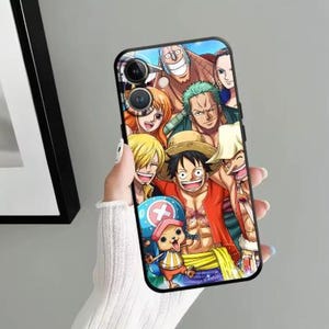Può includere: Custodia per telefono nera con un'illustrazione colorata dei personaggi dell'anime One Piece. Il design include Luffy, Zoro, Nami e altri membri dell'equipaggio. La custodia ha una finitura lucida e un bordo nero.