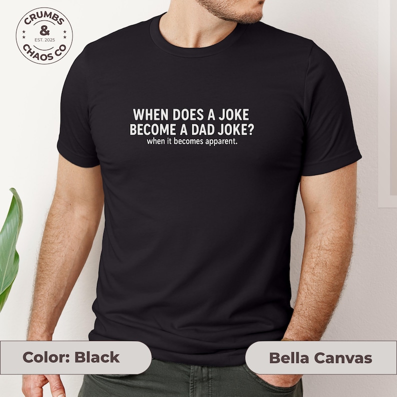 May include: Black t-shirt with the text "WHEN DOES A JOKE BECOME A DAD JOKE? when it becomes apparent." The shirt also features a small logo that says "CRUMBS & CHAOS CO EST. 2025". The shirt is made by Bella Canvas.