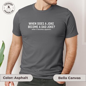May include: Asphalt-colored Bella Canvas t-shirt with the text "WHEN DOES A JOKE BECOME A DAD JOKE? when it becomes apparent." A circular logo with the text "CRUMBS & CHAOS CO EST. 2025" is visible on the upper left.