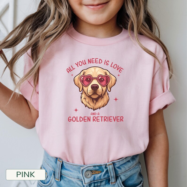 Puede incluir: Camiseta rosa claro con un dise&ntilde;o de Golden Retriever con gafas de sol en forma de coraz&oacute;n. El texto dice "ALL YOU NEED IS LOVE AND A GOLDEN RETRIEVER". La camiseta es de material suave y es adecuada para ni&ntilde;os.